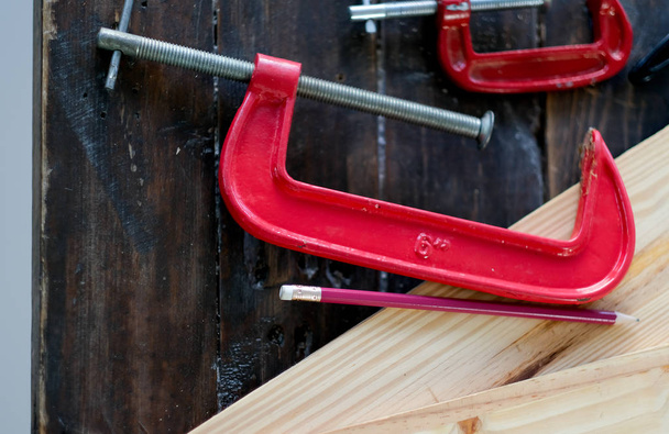 Zamknij widok czerwonego zacisku narzędzia do drewna rzemiosła pracy, który jest wprowadzony na drewniany stół z ołówkiem i innych urządzeń. - Zdjęcie, obraz