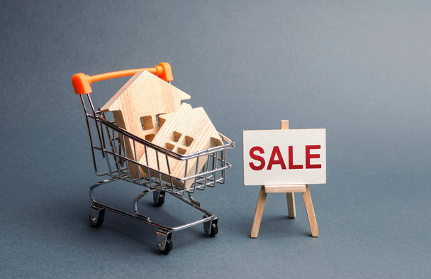 Two houses in a shopping cart and a stand with the inscription sale. selling a home. Announcement of the sale and attracting potential buyers. Advertising campaign. purchase of real estate. - Zdjęcie, obraz