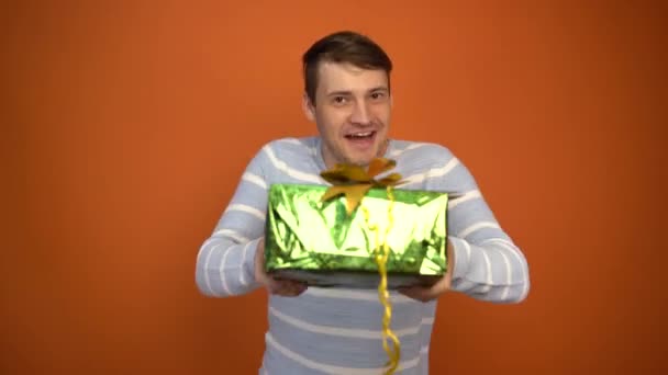 Sad handsome man received a gift and began to dance happily on an orange background. Holiday concept, holiday discounts, gifts and sales. - 映像、動画