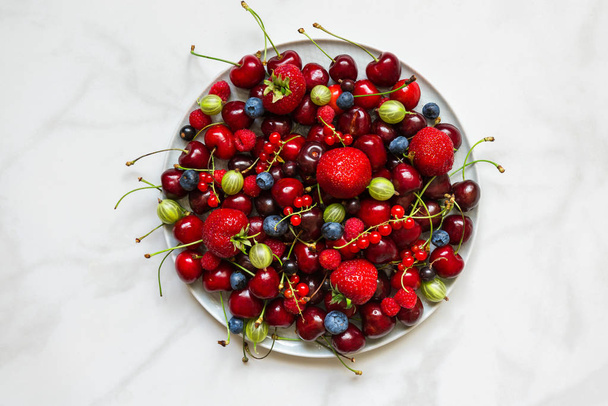 Various fresh summer berries in a plate on white marble table. - Fotó, kép