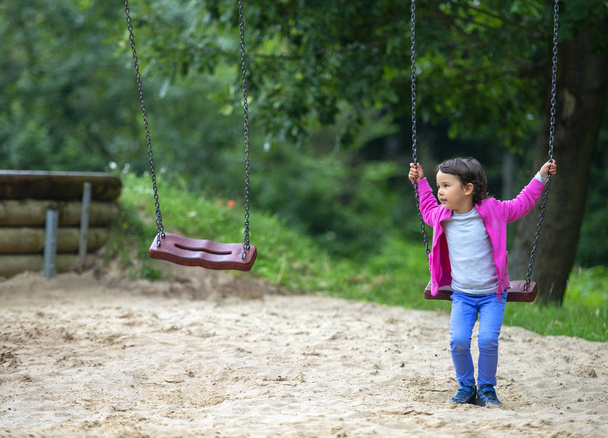 Nettes kleines Mädchen spielt auf Schaukel im Park - Foto, Bild