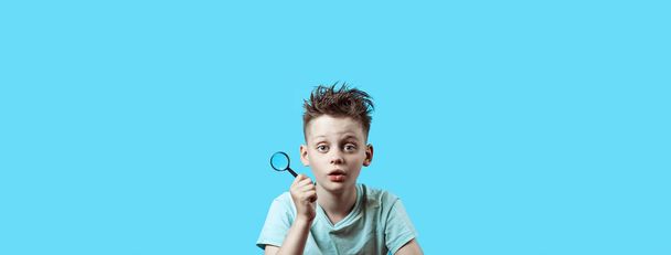 a boy in a light t-shirt holding a small magnifying glass on blue background - Foto, Imagem