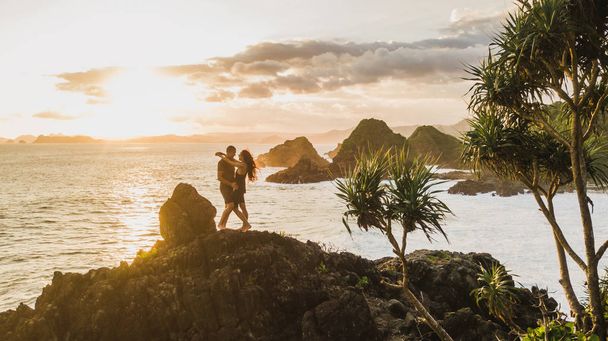 Casal desfrutando do pôr do sol com incrível vista para o oceano e montanha. Tra
 - Foto, Imagem