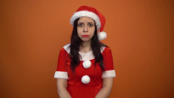 Smiling beautiful young woman in Santa Claus suit is holding a box with gifts on a orange background. Merry Christmas and Happy New Year. - Metraje, vídeo