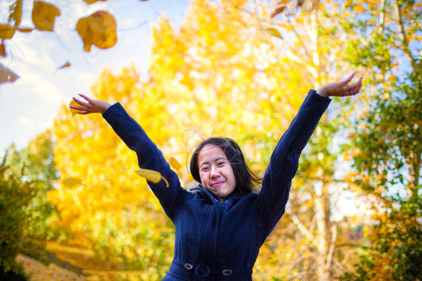 Asiática chica lanzando amarillo otoño hojas en el aire en el parque
 - Foto, imagen