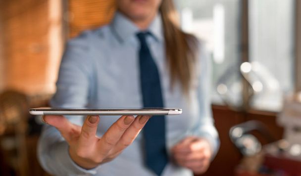 Blurred woman in the background holding mobile phone in the hand. Copy space with finger pointing in it. Business woman with shirt and tie in the background. - Photo, Image