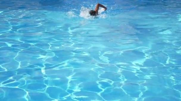 Sportlicher Junge schwimmt Freestyle in einem türkisfarbenen Planschteich in Zeitlupe Beeindruckende Sicht auf einen athletischen Teenager, der Freestyle professionell in einem Planschteich mit glitzernd türkisfarbenem Wasser in Zeitlupe schwimmt - Filmmaterial, Video