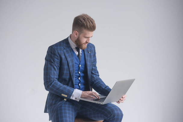 Seitenansicht eines konzentrierten Geschäftsmannes im Sessel, der am Laptop arbeitet - Foto, Bild
