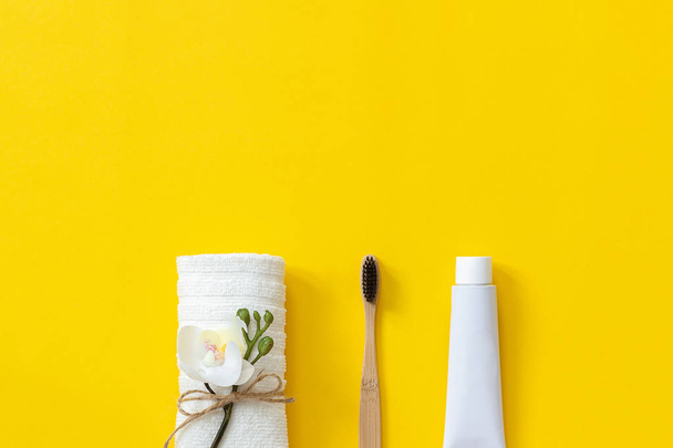 Natural eco-friendly bamboo brush, white towel and tube of toothpaste. Set for washing on paper yellow background. Copy space for text or your design Top view Flat lay - Fotó, kép