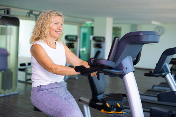 Spor salonunda bisikletle egzersiz mutlu yaşlı kadın. - Fotoğraf, Görsel