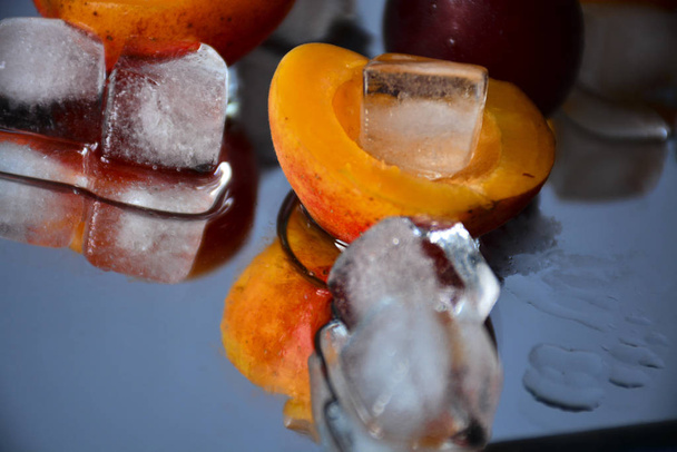 Meruňky a švestky se nacházejí na zrcadlovém povrchu s ledem. Voda z tavicího ledu a ovoce odraženého v zrcadle vytváří nádherné složení. Bílý LED kontrastuje s šťavnatou ovocem. - Fotografie, Obrázek