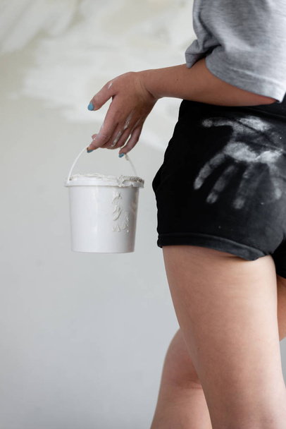 Uma foto de close-up de uma menina suja com massa branca segurando um balde contra um fundo de paredes de gesso
. - Foto, Imagem