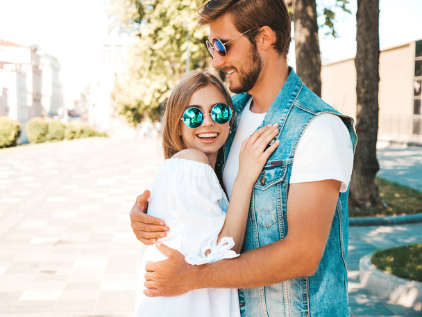 Smiling beautiful girl and her handsome boyfriend. Woman in casual summer dress and man in jeans clothes. Happy cheerful family. Female having fun on the street background.Hugging couple in sunglasses - Φωτογραφία, εικόνα