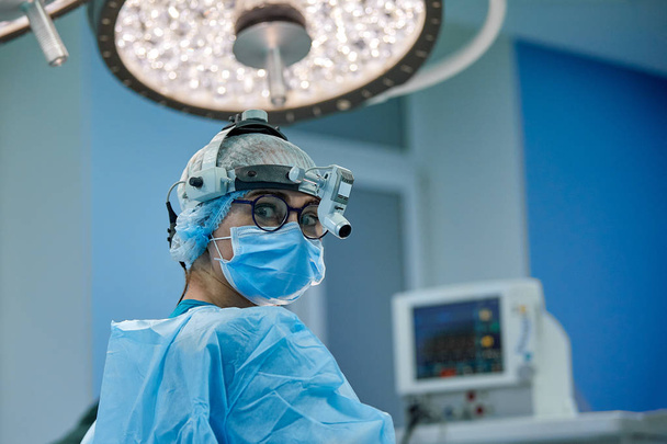 Close up portrait of female surgeon doctor wearing protective mask and hat during the operation. Healthcare, medical education, surgery concept. - Photo, Image