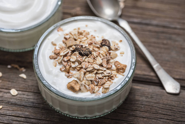 White yogurt in glass bowl with oatmeal on top on rustic wooden desk. - Photo, Image