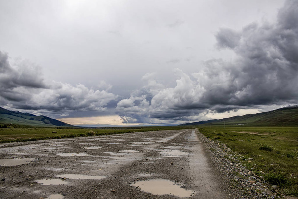 Strada di ghiaia che passa attraverso una valle di montagna sotto un cielo tempestoso
 - Foto, immagini
