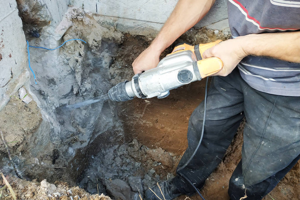 Trabalhador da indústria da construção civil usando broca de martelo pneumático para cortar a parede de tijolo de concreto, de perto
 - Foto, Imagem