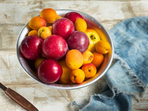 Fresh fruit nectarines, cream and apricots in a round plate on a blue denim napkin, composition on a bright table, a knife for cutting fruit, shot close-up - Photo, Image