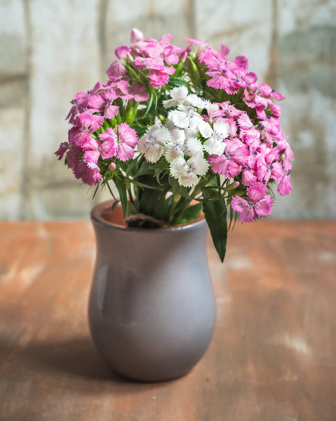 A bouquet of forest carnations in a gray clay vase on a bright table - Fotó, kép