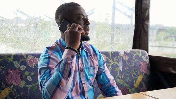 Afro homme américain appelle et parle smartphone assis dans un café en attente de sa commande
. - Photo, image