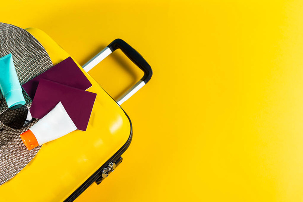 Яскрава та стильна валіза розміру кабіни з солом'яним капелюхом, сонцезахисним кремом та паспортами
 - Фото, зображення