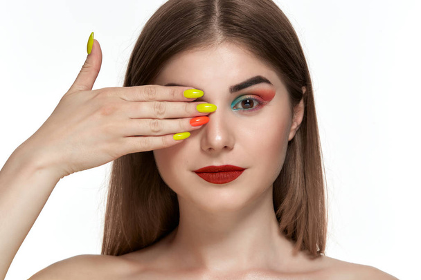 Κοντινό πορτρέτο της όμορφης νεαρής γυναίκας με φωτεινό χρώμα μακιγιάζ κρατώντας τα χέρια με φωτεινό μανικιούρ κοντά στο πρόσωπο - Φωτογραφία, εικόνα