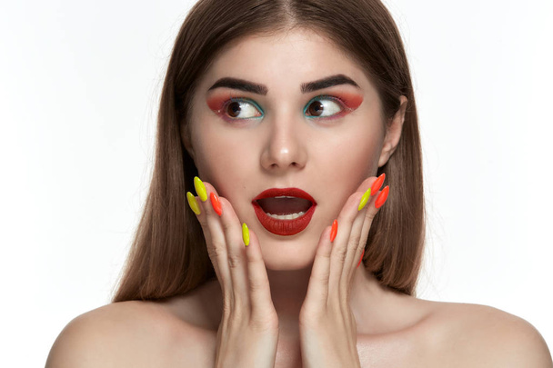 Closeup portrait of beautiful young woman with bright color make-up holding hands with bright  manicure close to face - Photo, Image