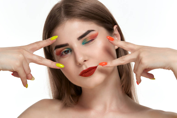 Closeup portrait of beautiful young woman with bright color make-up holding hands with bright  manicure close to face - Photo, Image