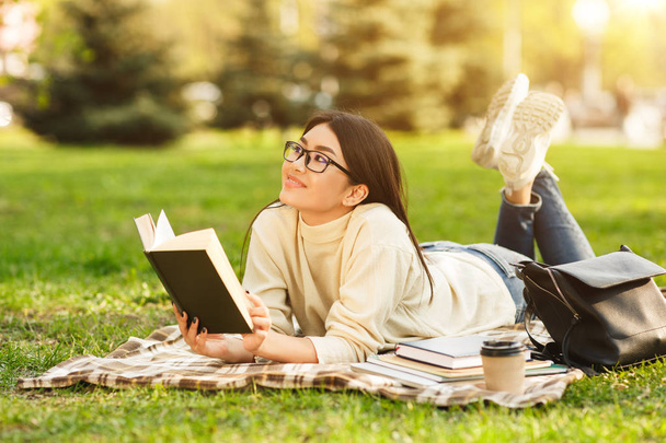 Dreamy student girl reading book, resting in park - Photo, Image
