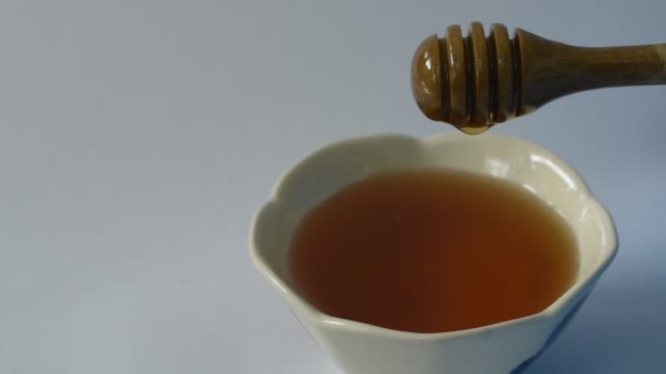 白い背景でカップに木製のスクープドロップの蜂蜜 - 映像、動画