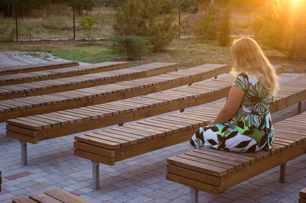Το κορίτσι που κάθεται μόνη στην πλάτη της ανάμεσα σε πολλά παγκάκια - Φωτογραφία, εικόνα