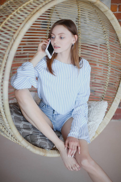 Young pretty girl is sitting in chair and talking on phone - Foto, afbeelding