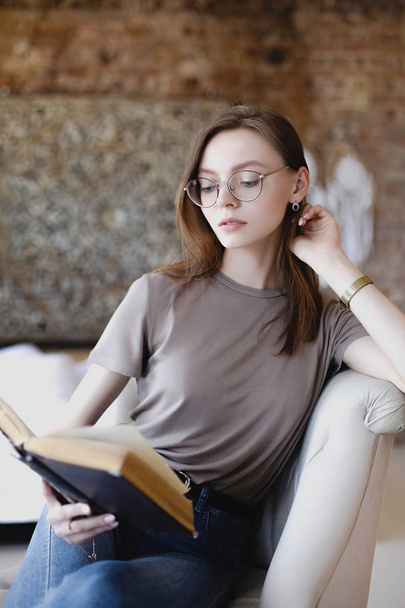 Young sweet girl with glasses sits and reads book - Valokuva, kuva