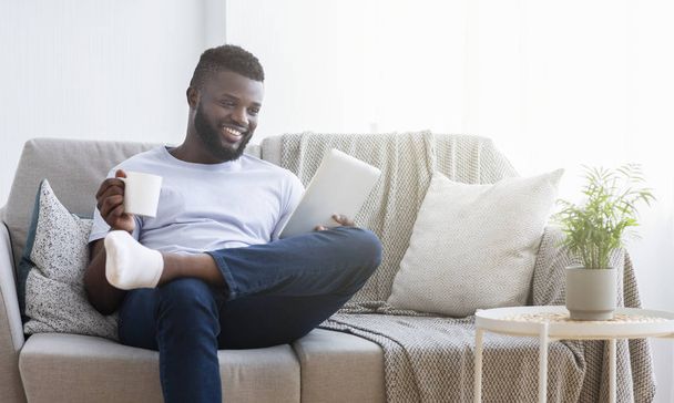 afro-americano millennial cara lendo notícias no tablet e tomar café
 - Foto, Imagem