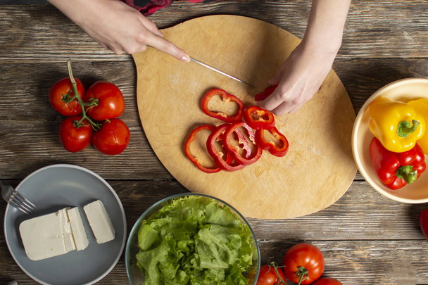 mains d'une jeune fille coupé poivron sur une table en bois, le processus de fabrication de salade végétarienne, coupe en gros plan de légumes
 - Photo, image