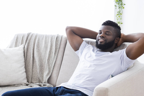 Szczęśliwy afrykański facet relaks w domu, siedząc na kanapie z zamkniętymi oczami - Zdjęcie, obraz