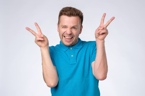 young man in blue polo shirt showing the victory sign and looking at the camera - Foto, Imagen
