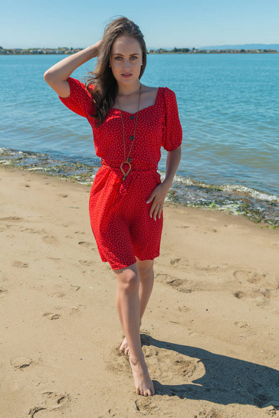 Brunette in red on a beach - Фото, изображение