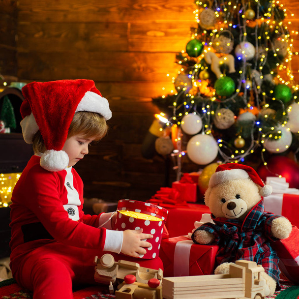 Ευτυχισμένο παιδί με Χριστουγεννιάτικο κουτί δώρου. Ένα μικρό αγόρι με ζεστά ρούχα που κάθεται και παίζει με τα ξύλινα παιχνίδια δώρο. Χριστουγεννιάτικο θαύμα και νέα χρόνια αισθήματα. Ανοιχτά παιχνίδια. Πρώτη ανάμνηση της παιδικής ηλικίας. - Φωτογραφία, εικόνα