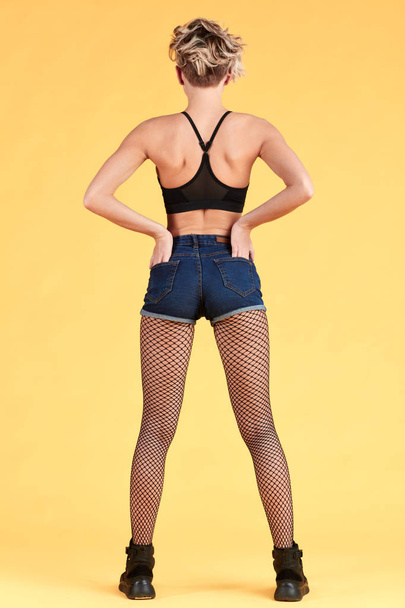 Sexy woman with hands on her pockets. Studio shot on yellow background. - 写真・画像
