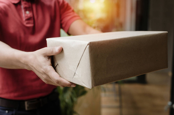 hand of young delivery service man in red uniform to customer receiving parcel post box from courier at home, cargo shipping, express delivery service, online shopping and logistics concept - 写真・画像