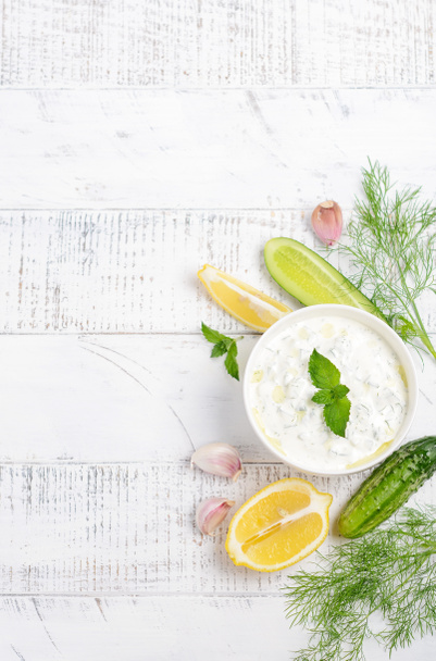 Yunan dip sosu veya soyunma tzatziki ve malzemeler beyaz ahşap masa üzerinde zeytinyağı ve nane ile dekore  - Fotoğraf, Görsel