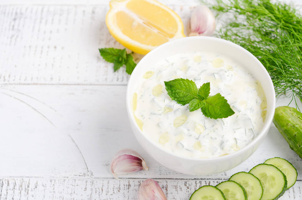 Greek dip sauce or dressing tzatziki and ingredients decorated with olive oil and mint on white wooden table  - Photo, Image