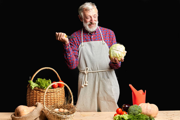 Cheerful senior farmer having fun during cooking healthy lunch for his friends - Foto, imagen