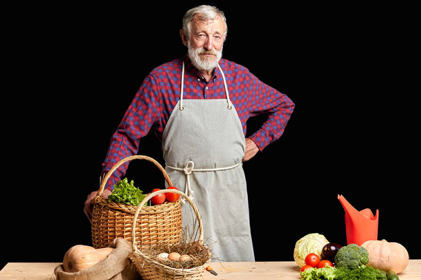 Mature farmer wants to have some rest after working day, stands near vegetables - Фото, изображение