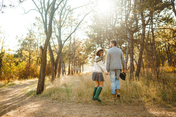 Lovely hipster couple looking at each other. Couple wearing beautiful hats and sweaters. Lifestyle, happy couple of two play on a sunny day in the park. The concept of youth, love and lifestyle. Sunset in autumn  - Photo, Image
