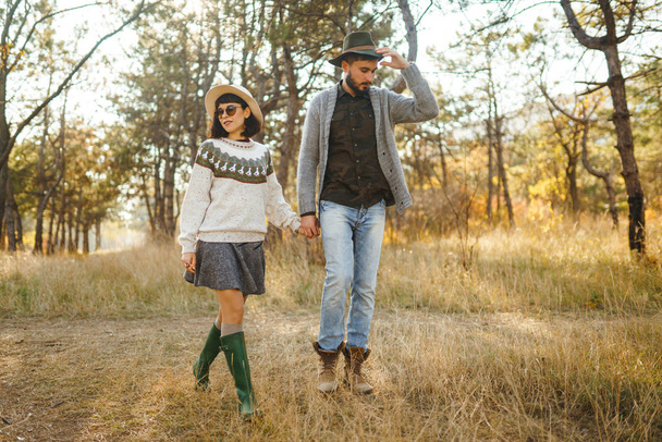 Lovely hipster couple looking at each other. Couple wearing beautiful hats and sweaters. Lifestyle, happy couple of two play on a sunny day in the park. The concept of youth, love and lifestyle. Sunset in autumn  - Photo, image