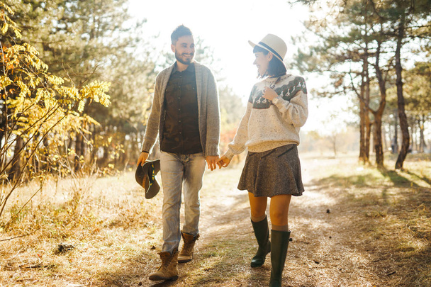 Lovely hipster couple looking at each other. Couple wearing beautiful hats and sweaters. Lifestyle, happy couple of two play on a sunny day in the park. The concept of youth, love and lifestyle. Sunset in autumn  - Foto, immagini