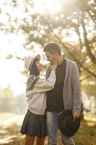 Lovely hipster couple looking at each other. Couple wearing beautiful hats and sweaters. Lifestyle, happy couple of two play on a sunny day in the park. The concept of youth, love and lifestyle. Sunset in autumn  - Photo, Image