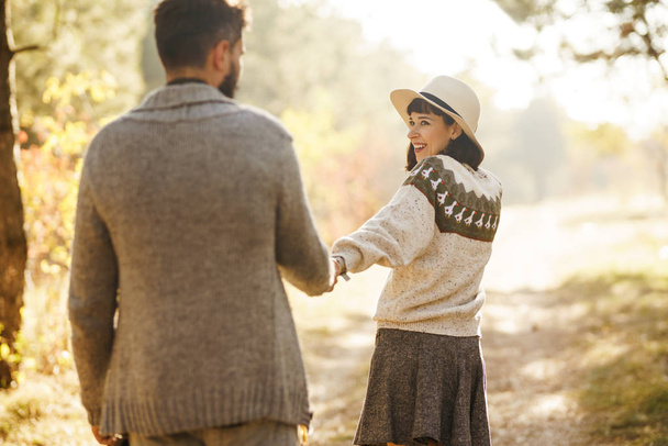 Lovely hipster couple looking at each other. Couple wearing beautiful hats and sweaters. Lifestyle, happy couple of two play on a sunny day in the park. The concept of youth, love and lifestyle. Sunset in autumn  - Foto, imagen